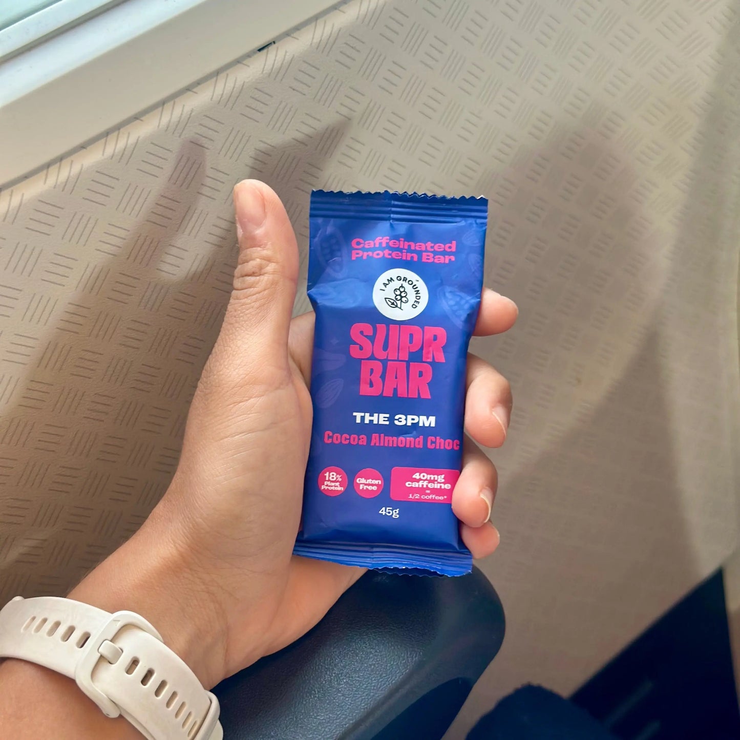 Hand holding a blue Super Bar packaging in an airplane seat