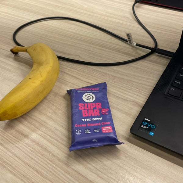 Blue protein bar, banana, and laptop on a desk with text overlay.