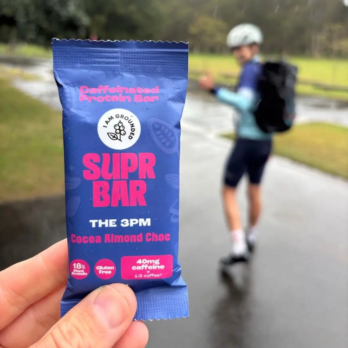 Supr Bar protein bar held in front of a blurred background of a person on a skateboard.