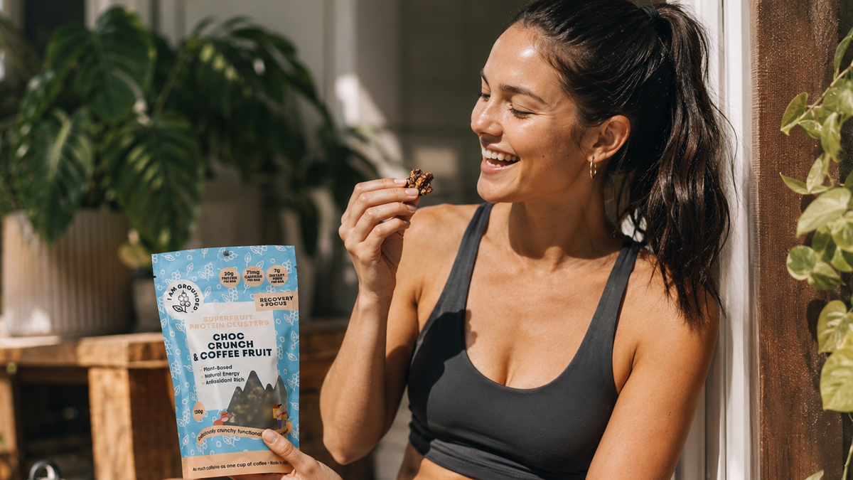 Woman in athletic wear holding a snack and a package outdoors with plants in the background