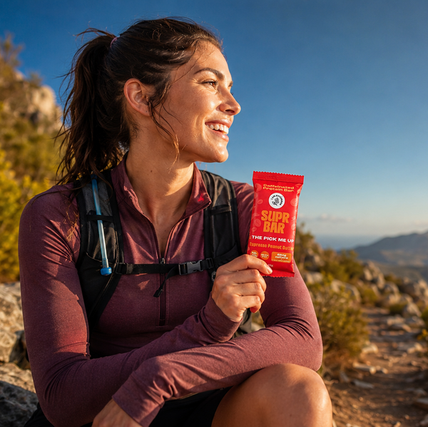 Woman in hiking attire holding a red packet on a mountain trail with scenic view.